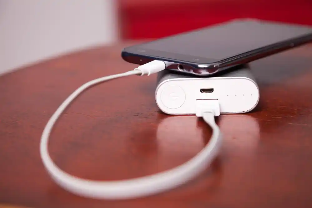 Smartfon podłączony do ładowarki leżący na biurku obok kabla i zasilacza